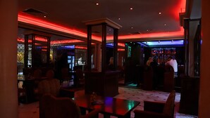 A dimly lit bar area with red and blue lighting, wooden furniture, and a bar counter. - Legend Hotel (Beirut)