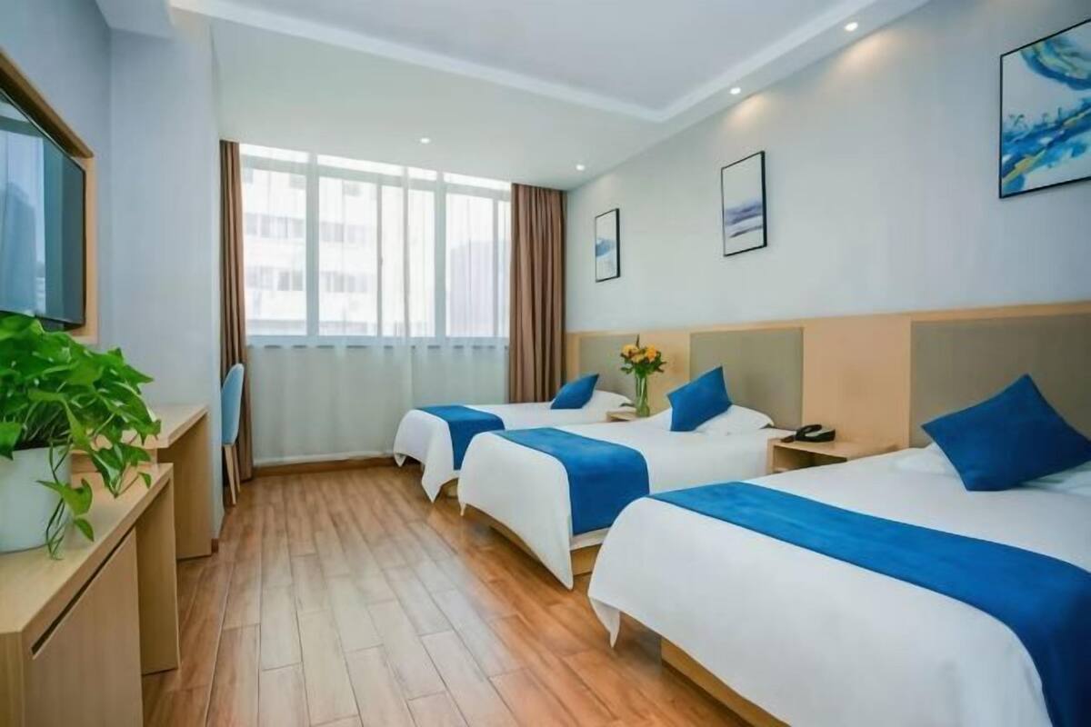 A hotel room with two beds, a TV, a desk, and a window with curtains.