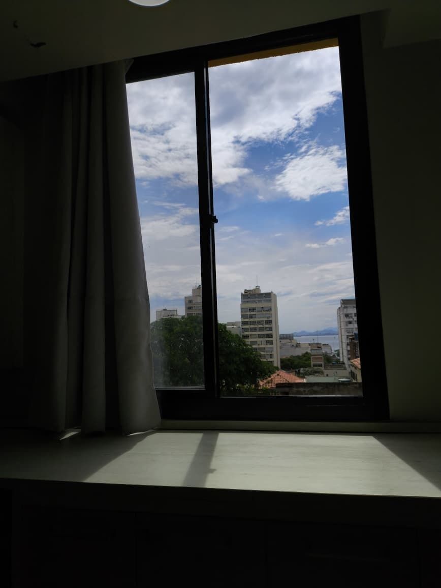 A room with a large window, curtains, and a view of buildings and trees.
