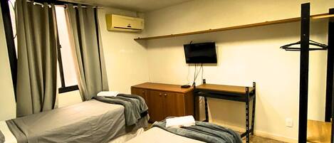 Habitación de hotel con dos camas, un escritorio, un televisor y aire acondicionado.