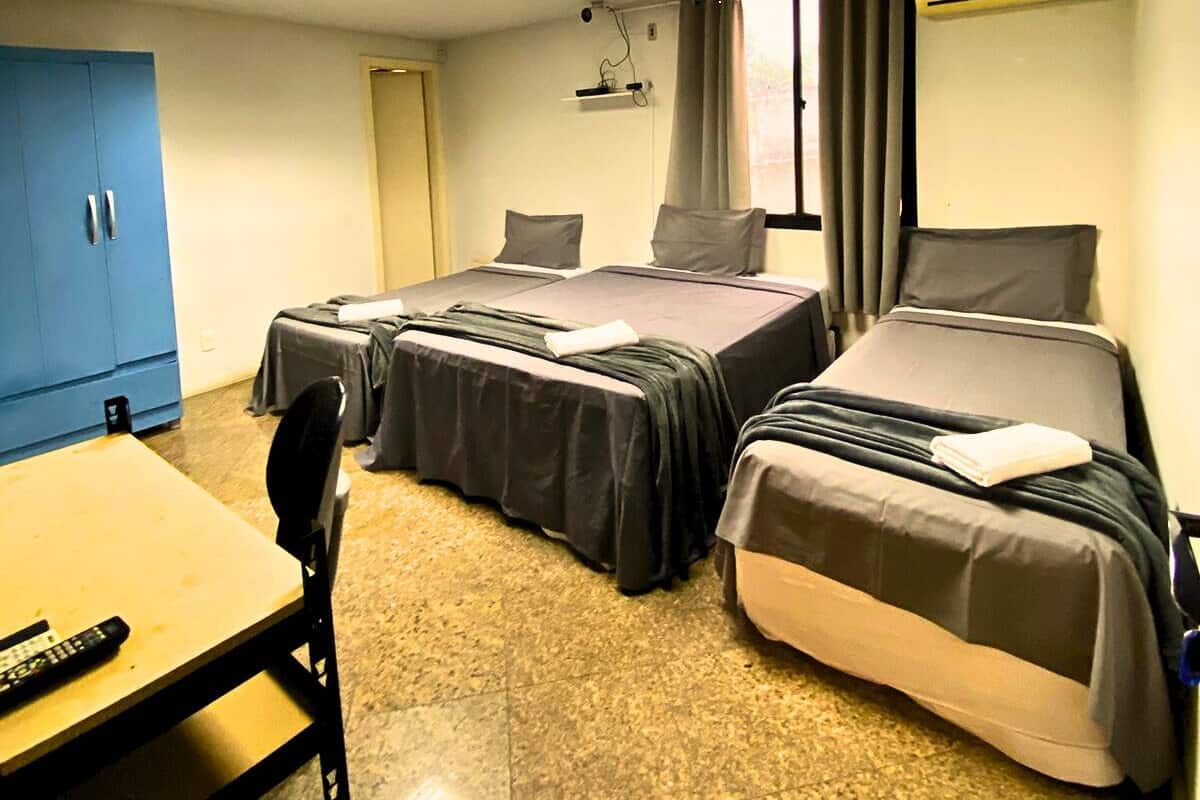 Habitación de hotel con dos camas, un escritorio y una silla. Hay una ventana con cortinas, una lámpara del techo y un equipo de aire acondicionado.