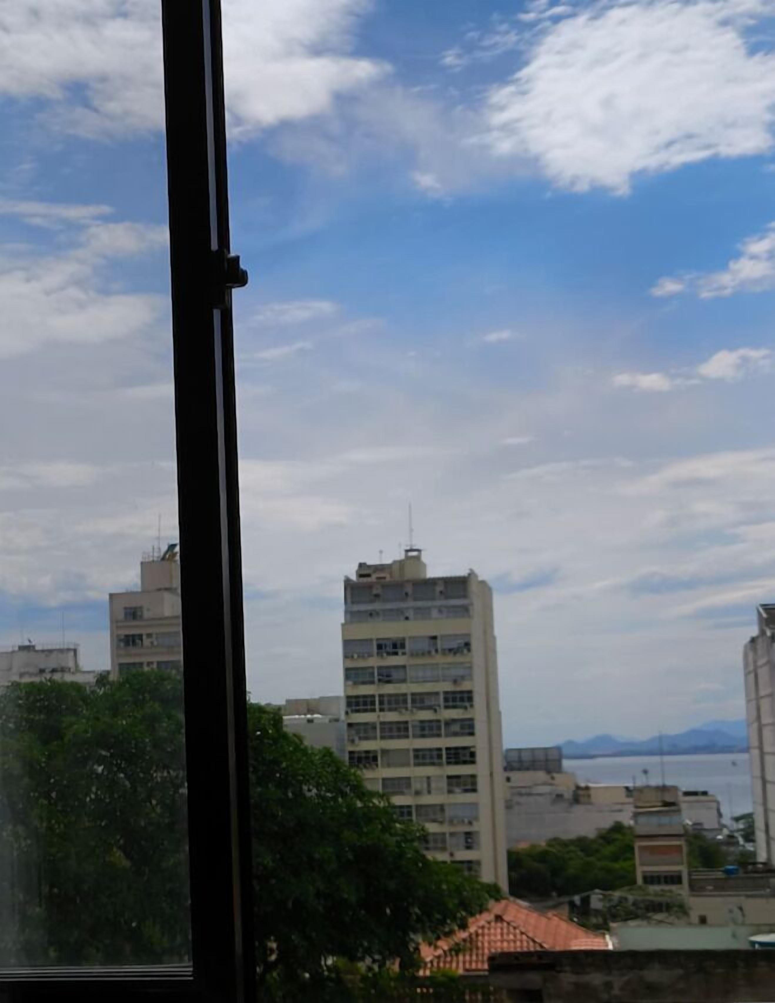 Vista pela janela de um horizonte urbano com edifícios e uma massa de água ao longe.