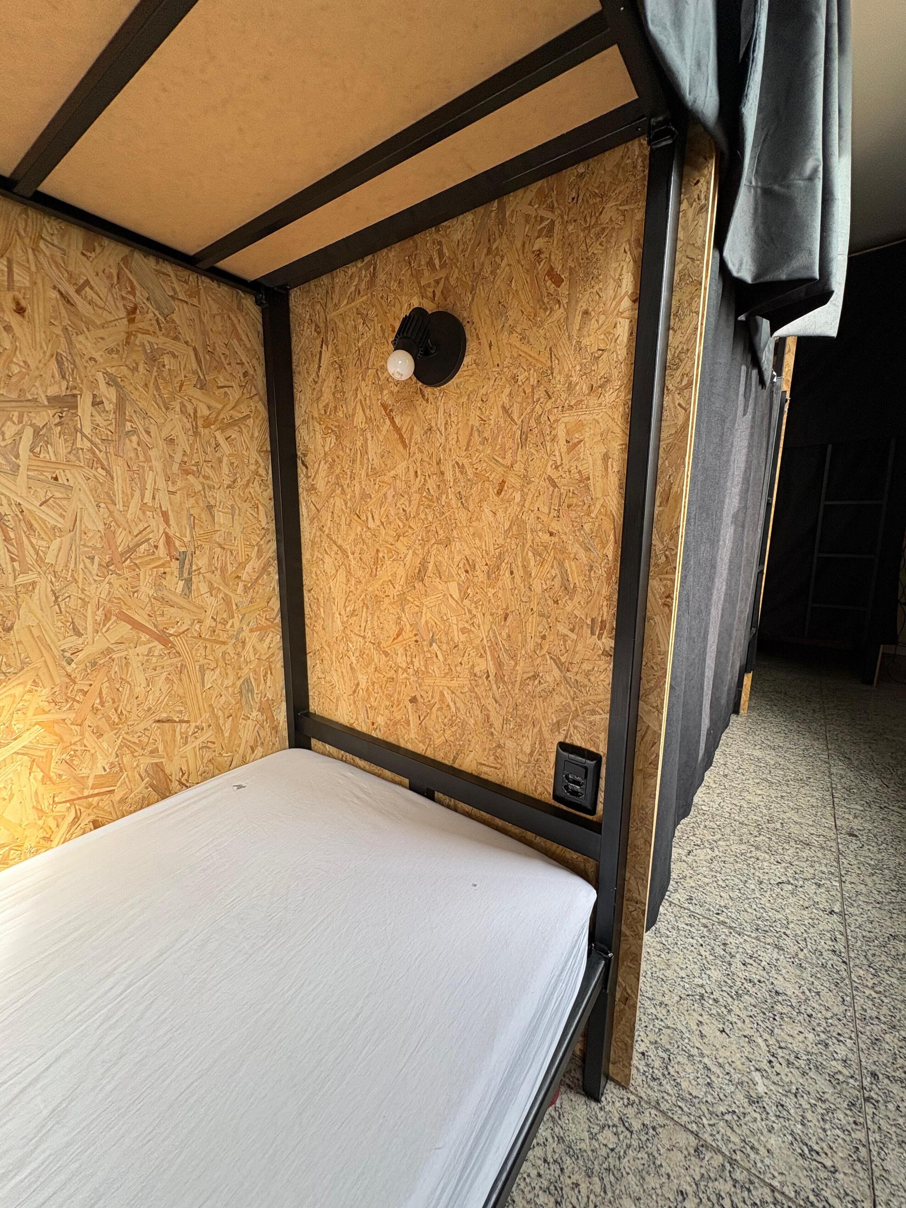 Una cama litera con colchón, una lámpara fijada a la pared y un enchufe.