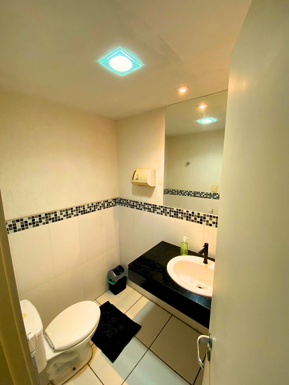 A bathroom with a white toilet, a black sink, a mirror, and a tiled backsplash.