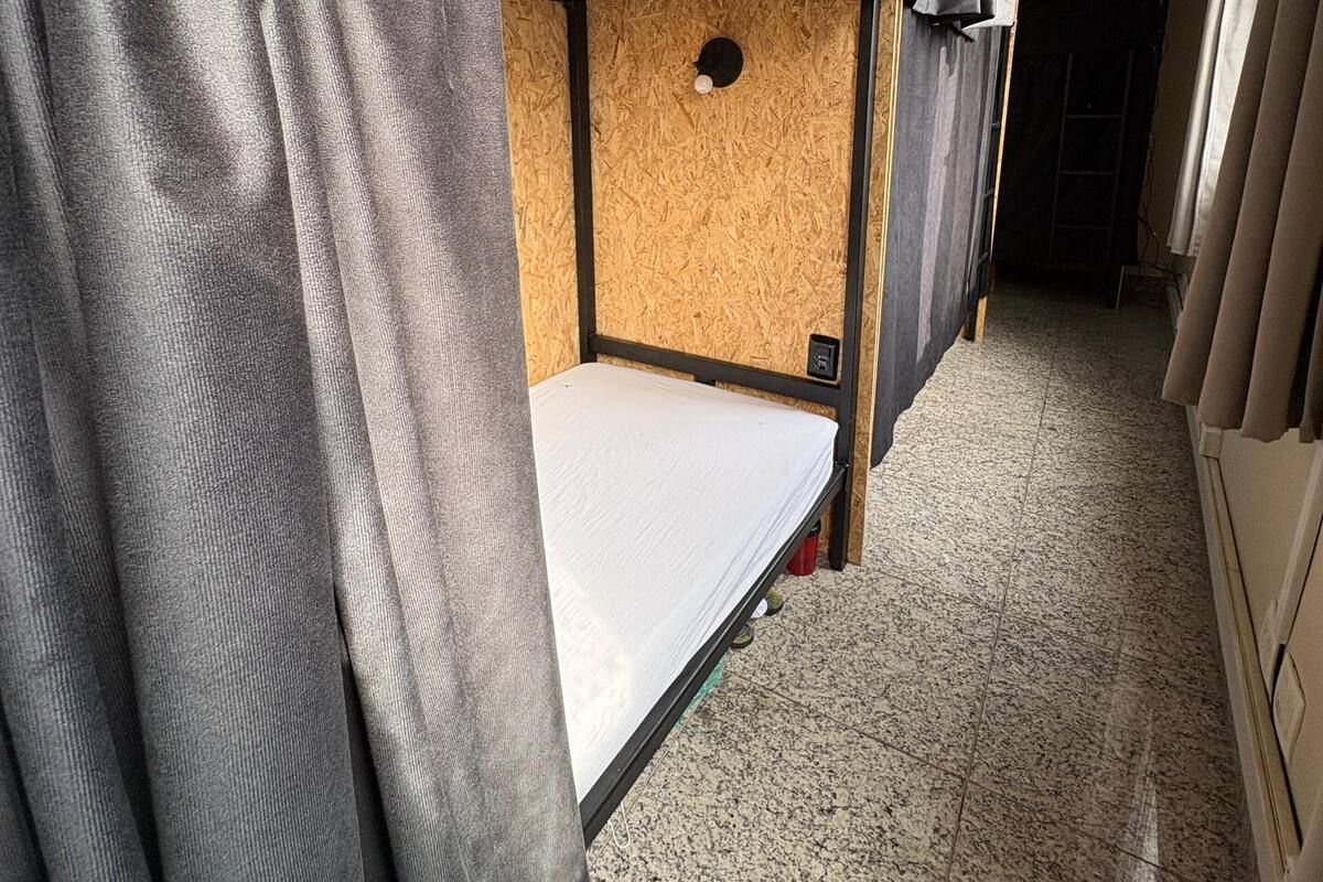 Habitación con literas de madera, un colchón y una cortina.