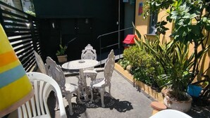An outdoor seating area with white plastic chairs and tables, a sign for "M C OFFICE HOSTEL," and potted plants. - MEC Office Hostel (Niteroi)