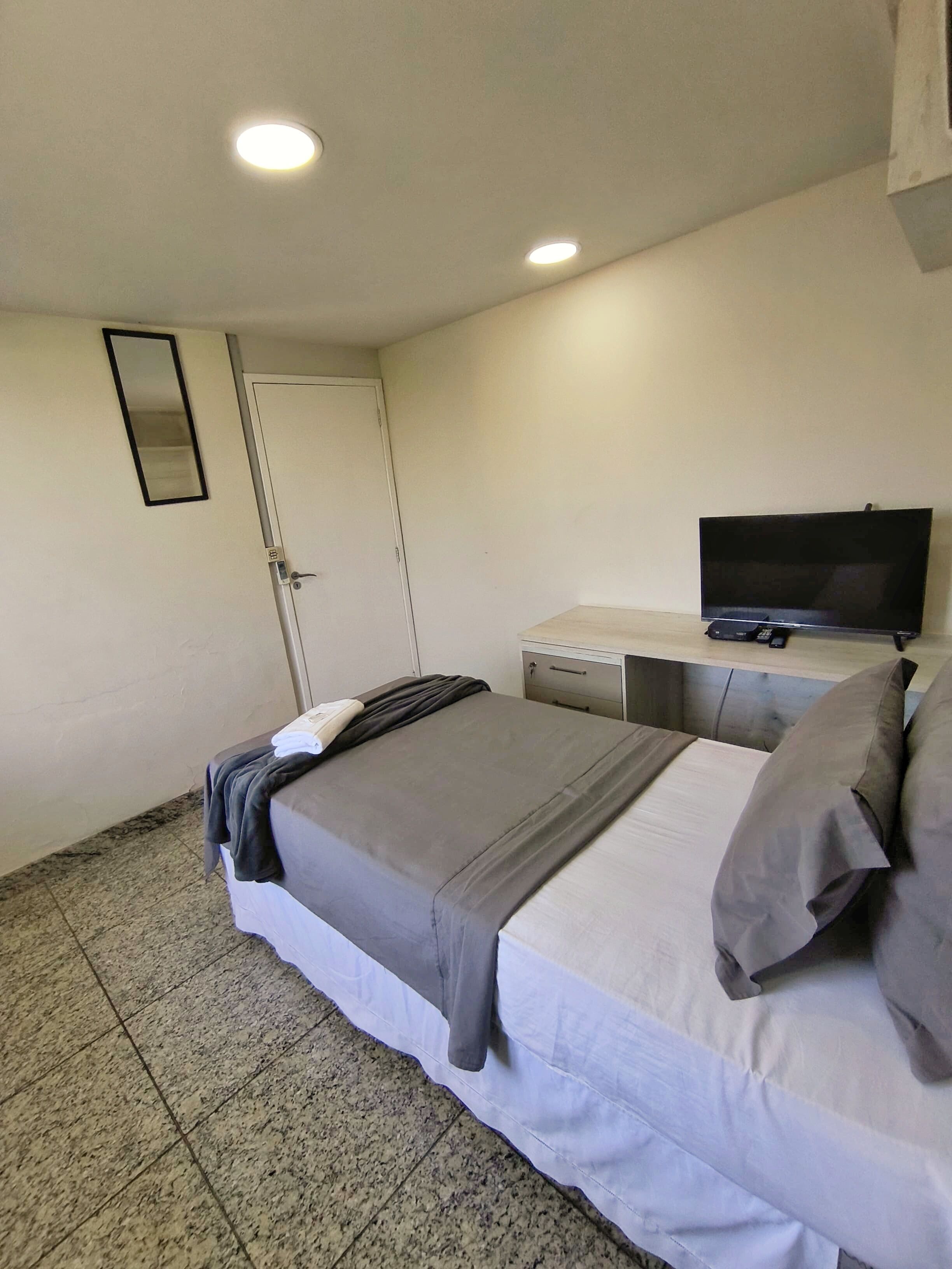 A hotel room with a bed, a television, a desk, and a door.
