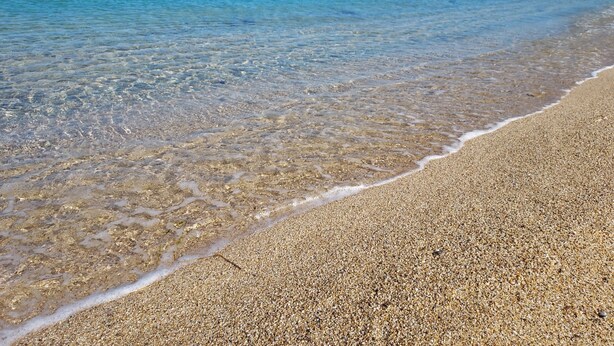 A beach with clear shallow waters and a pebbly shore.
