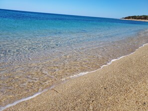 A beach with clear shallow waters and a pebbly shore.