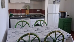 A compact kitchen with a dining table, chairs, a hanging light fixture, and basic appliances.