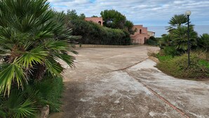A paved pathway leading to a building with a pink facade, surrounded by lush greenery and overlooking a body of water.