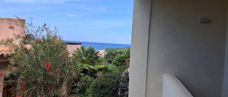 A balcony with a view of a garden and the sea.