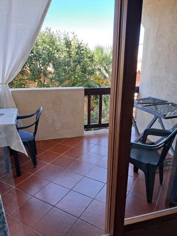 A balcony with a table and chairs, a metal rack, and a view of greenery.
