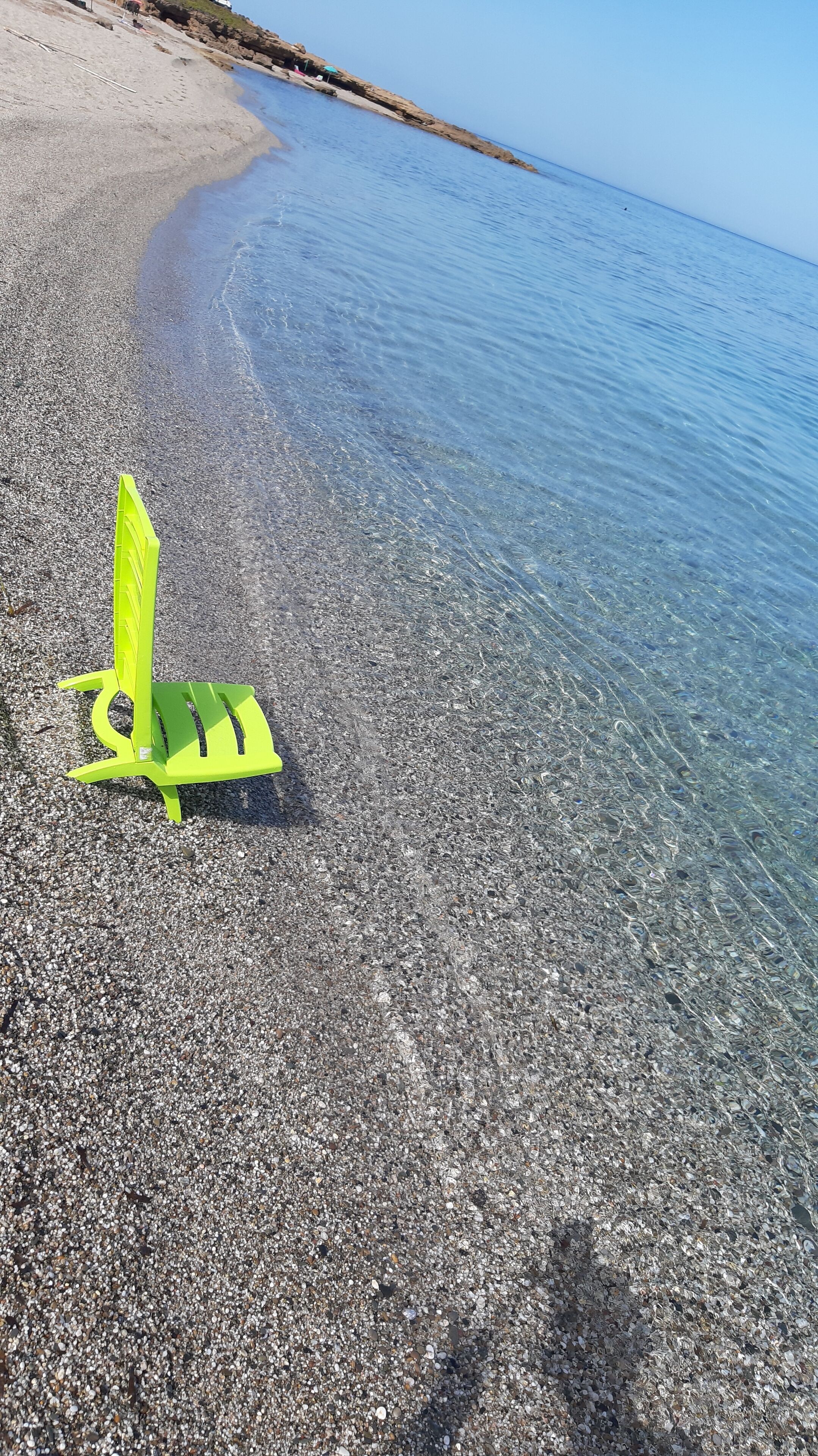 Una playa despejada con una silla amarilla brillante cerca de la orilla.