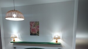A bedroom with a bed, two wall-mounted lamps, a shelf with a painting, and a green headboard.