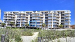 A beachfront hotel with multiple balconies, a sandy beach in front, and a clear blue sky. - Oceanfront 2Bed 2Bath Condo with Large Balcony & Amazing views  (North Myrtle Beach)