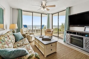 A spacious living room with a ceiling fan, a flat-screen TV, a sofa, a coffee table, and a balcony with a view of the beach. - Oceanfront 2Bed 2Bath Condo with Large Balcony & Amazing views  (North Myrtle Beach)