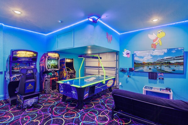 Une salle d’arcade avec des néons, une table de billard et des bornes d’arcade.