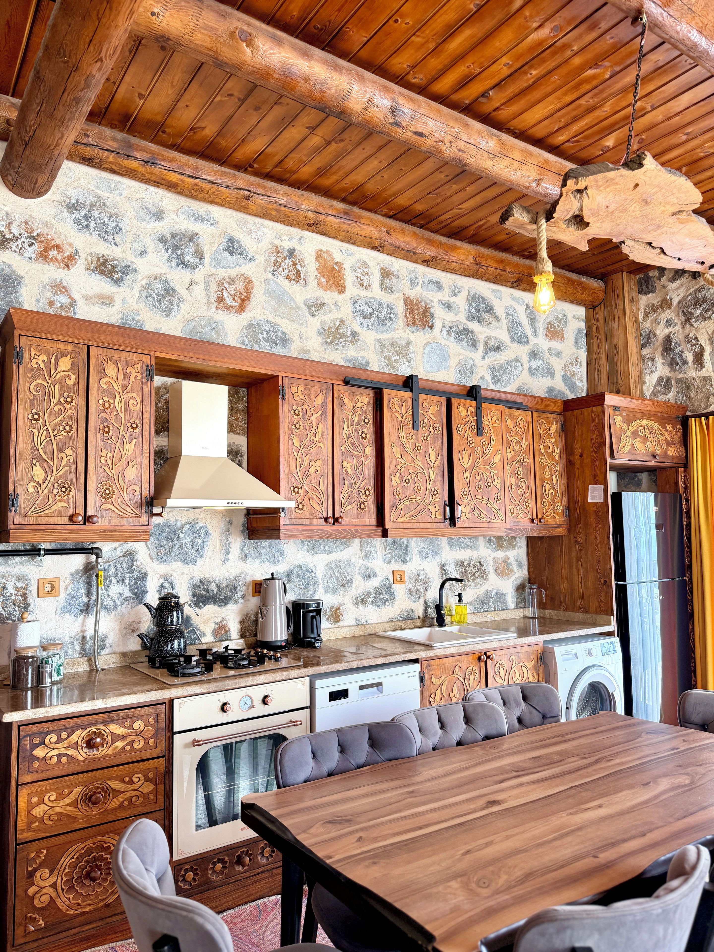 A rustic kitchen with stone walls, wooden cabinets, and a dining area with a wooden table and chairs.