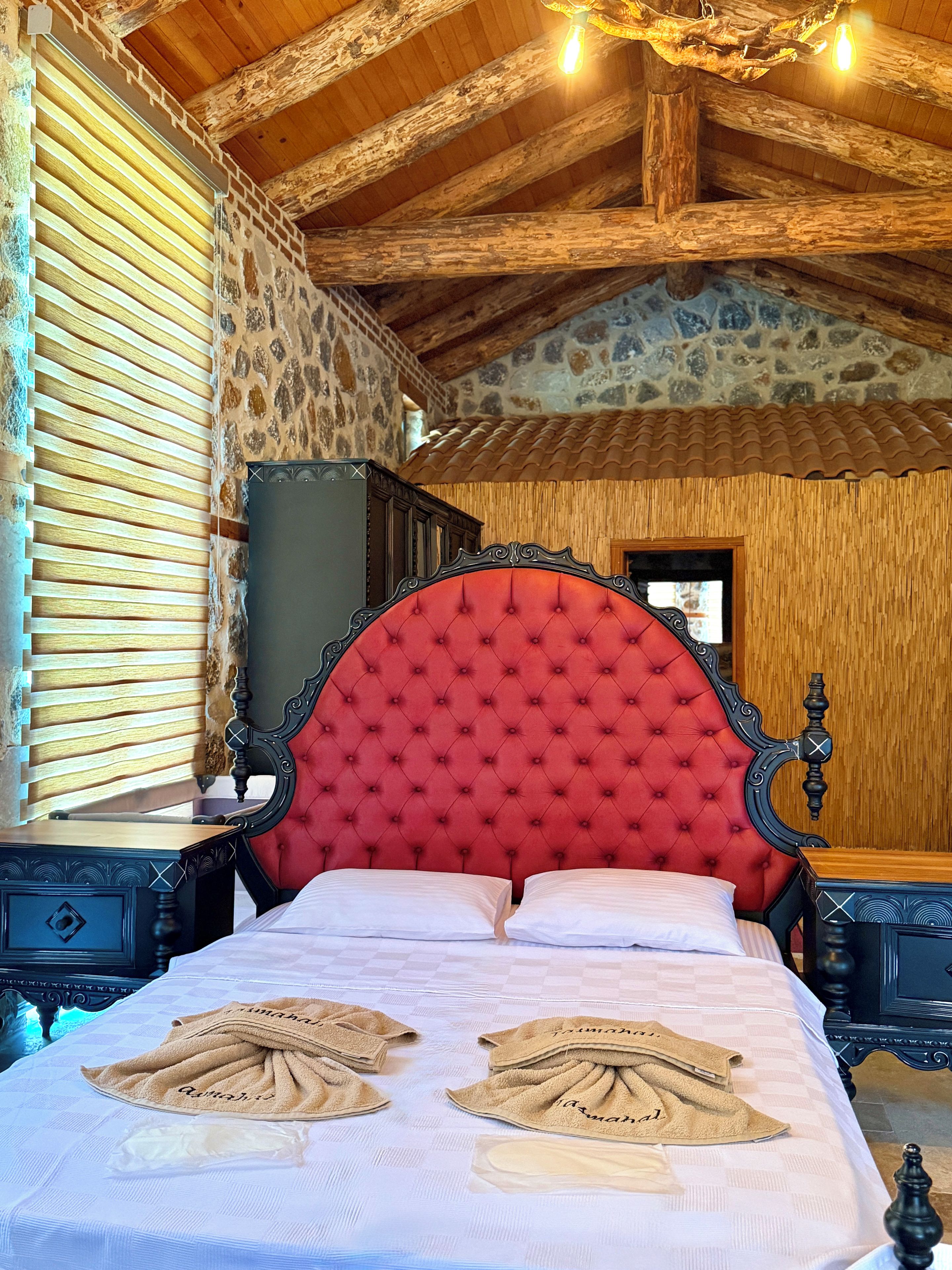 A room with a large bed, wooden headboard, and a stone wall.