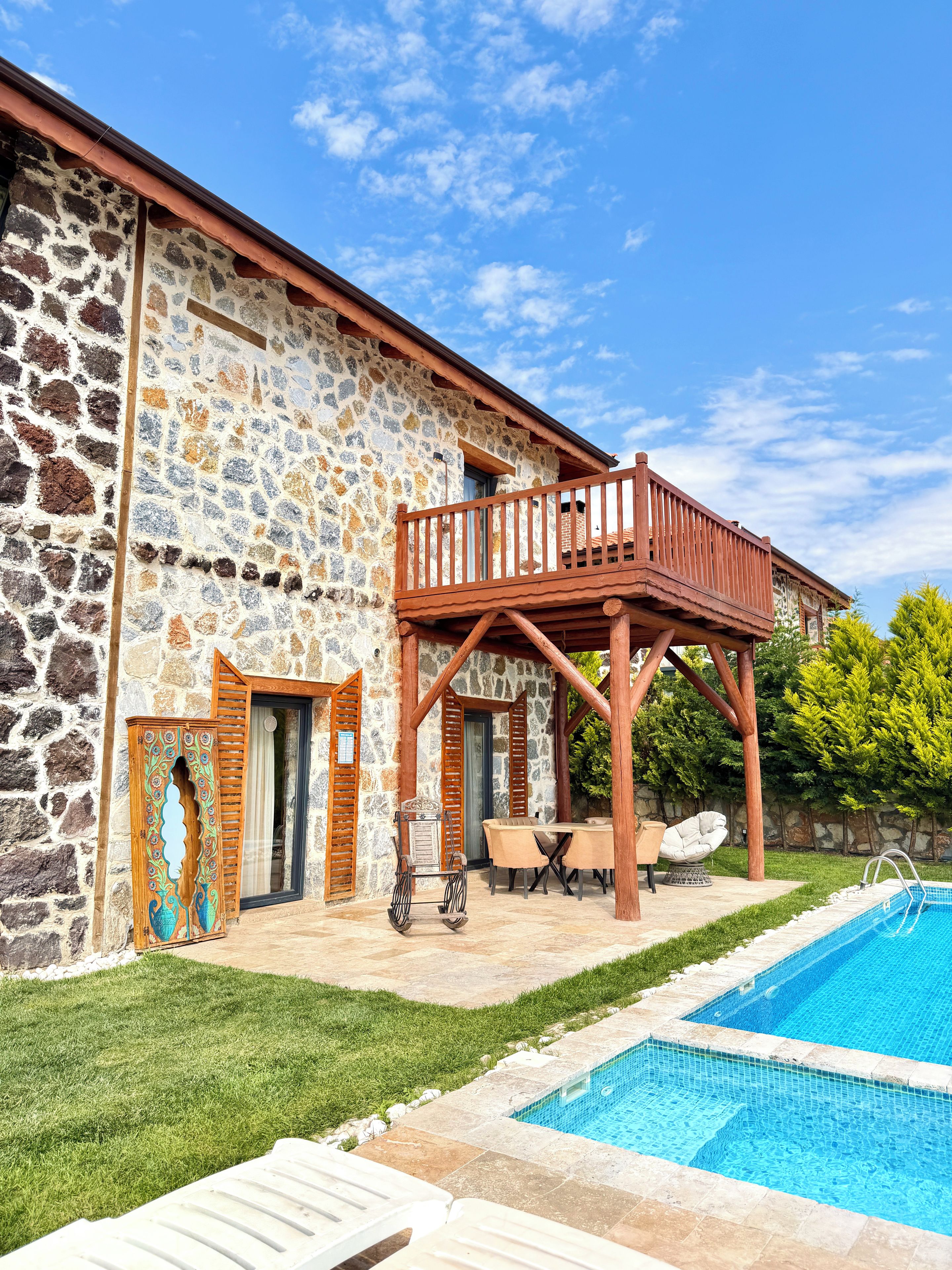 Um edifício de pedra com um deck de madeira, piscina e gramado.