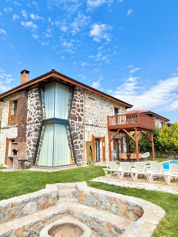 Un edificio de piedra con un ventanal grande, un balcón y una piscina.