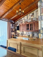 Una cocina rústica con pared de piedra, armarios de madera y techo de madera.