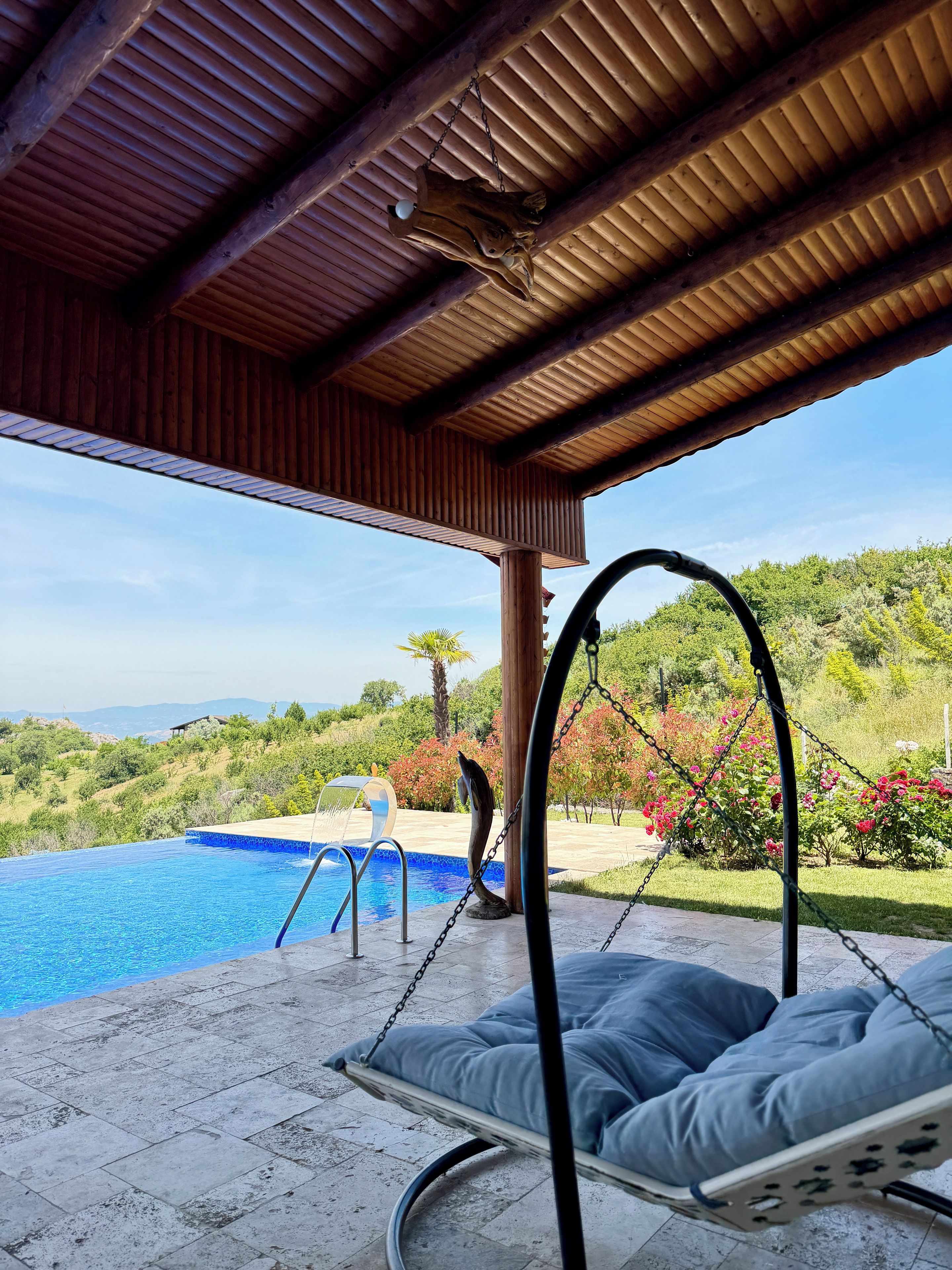 A covered outdoor area with a pool, a swing chair, and a view of the landscape.