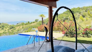 Un espacio al aire libre techado con piscina, una silla colgante y vistas al paisaje.