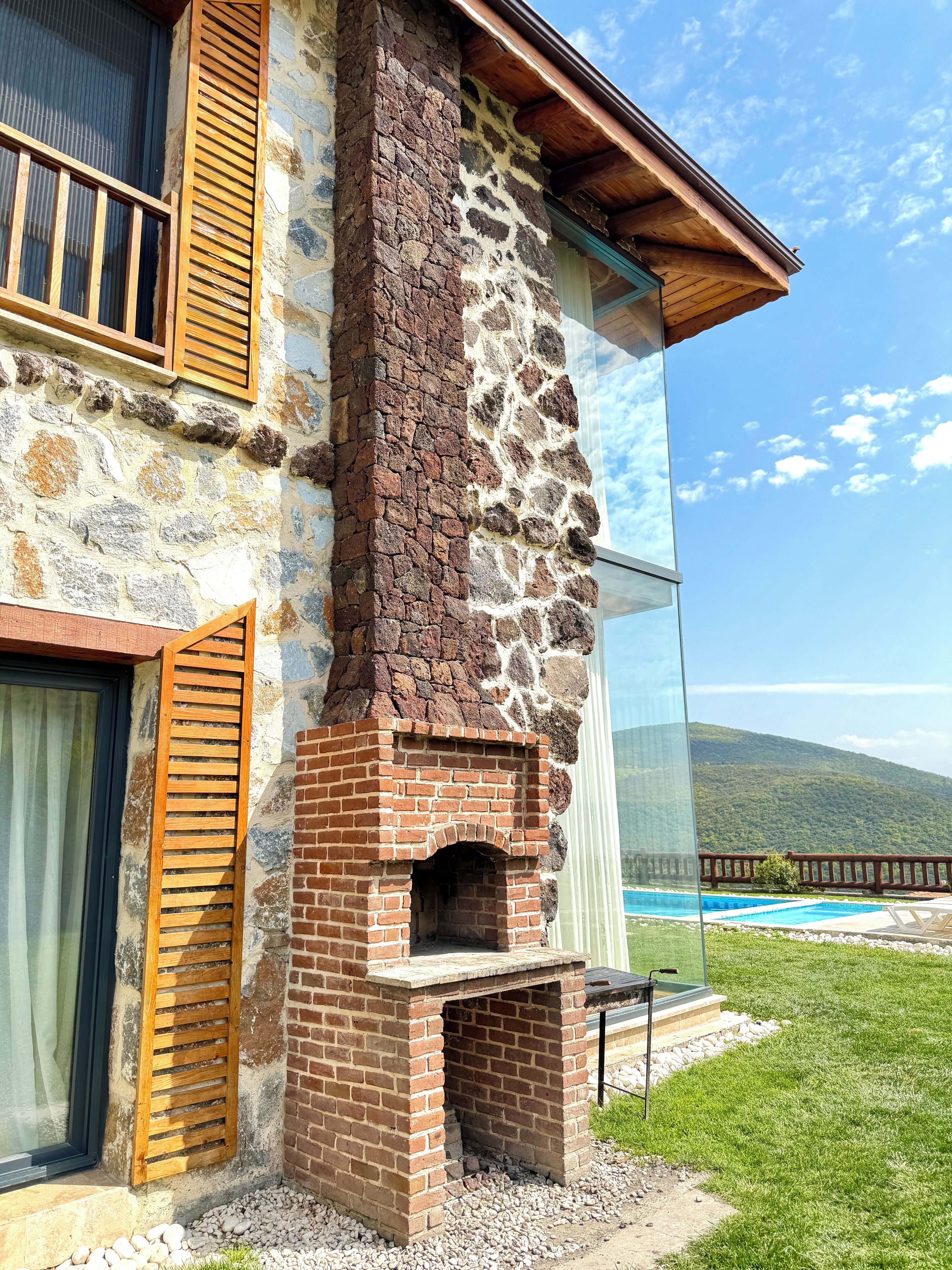 Edificio de piedra con chimenea de ladrillo, un persiano de madera y vistas a una piscina.