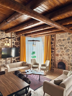 Una sala de estar acogedora con pared de piedra, vigas de madera en el techo, chimenea y televisor de pantalla plana.