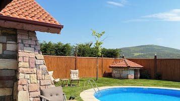 Un jardin avec une piscine, un mur en pierre, une terrasse en bois et du mobilier d’extérieur.