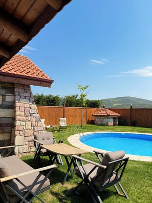 Un patio trasero con piscina, muro de piedra, terraza de madera y mobiliario exterior.