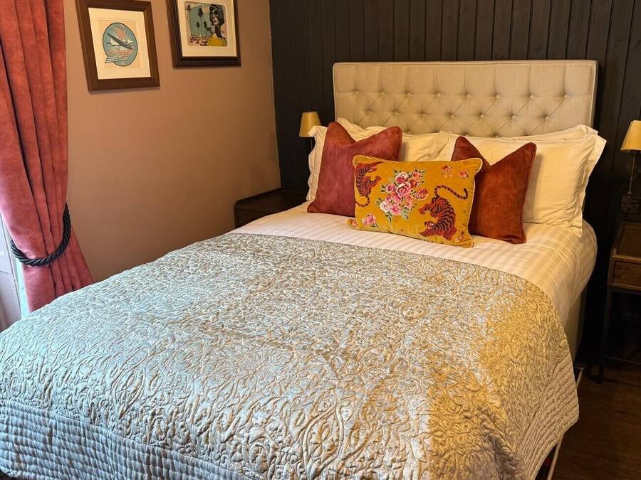 Una cama bien hecha con un edredón estampado, un cabecero acolchado y varias almohadas.