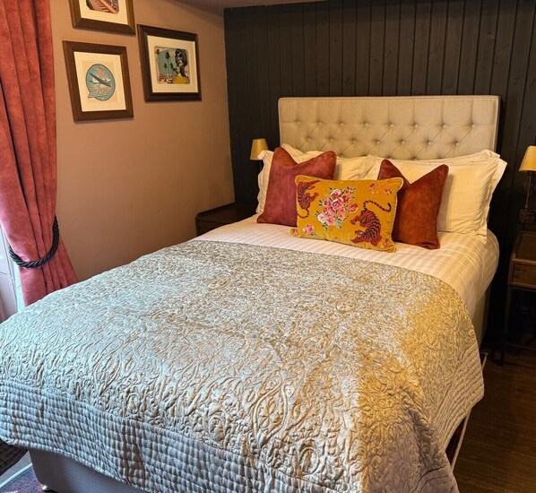 Una cama bien hecha con un edredón estampado, un cabecero acolchado y varias almohadas.