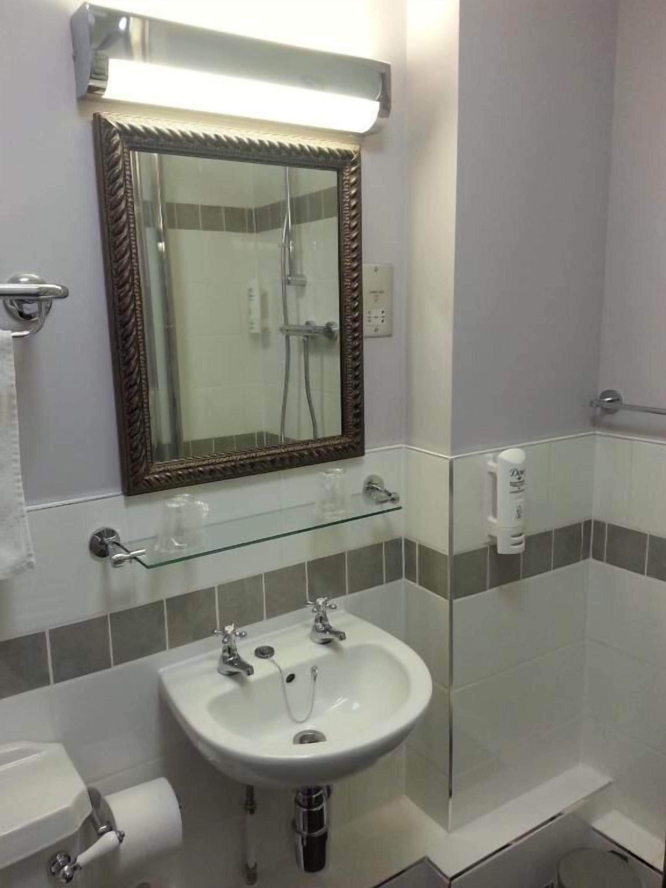 Un bagno con box doccia in vetro, un lavandino bianco con specchio sopra e uno scaffale in vetro.