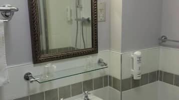 Un baño con cabina de ducha de vidrio, un lavabo blanco con espejo y un estante de vidrio.