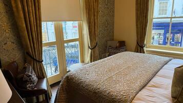 A bedroom with a large bed, a chair, and a view of the street through a window.