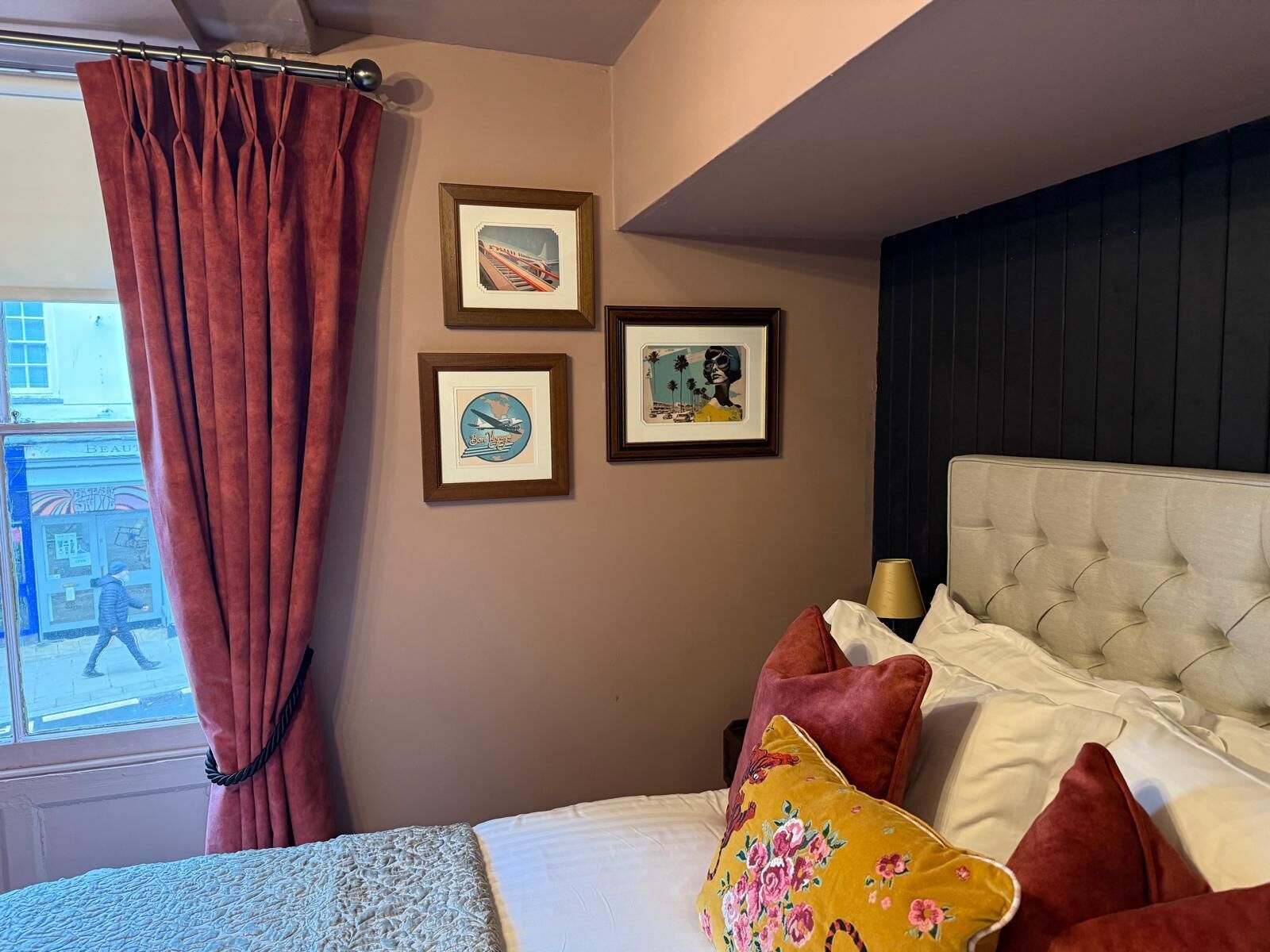 Ein Schlafzimmer mit einem Bett, einem Fenster mit Vorhängen und drei gerahmten Bildern an der Wand.