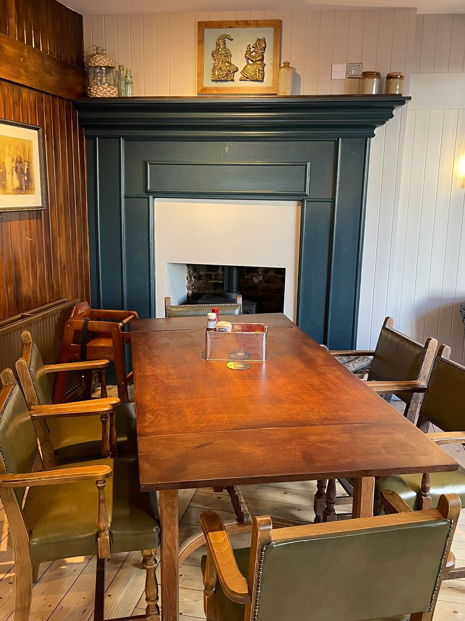 Une table de salle à manger en bois, des chaises, une cheminée et des objets décoratifs sur le manteau de la cheminée.