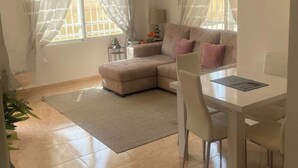Een moderne woonkamer met een modulaire bank, een eettafel met stoelen en een plafondventilator.