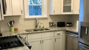 A kitchen with white cabinets, a stainless steel refrigerator, a gas stove, a window with a view, and a rug on the floor. - ✽ Charming Cottage ✽ close to College/Town/Station (Wheaton)