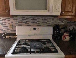 Une cuisine avec un four blanc, un four à micro-ondes placé au-dessus, et un mur recouvert de carreaux.