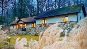 A stone house with a sloped roof and a stone foundation, surrounded by tall grasses and trees. - Appalachian Mountain Inn (Mill Run)