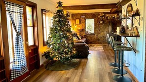 A cozy living room with a decorated Christmas tree, a stone fireplace, and a bar area with stools. - Appalachian Mountain Inn (Mill Run)