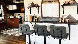 A bar area with a wooden counter, three bar stools, and a mirror above the counter. - Appalachian Mountain Inn (Mill Run)