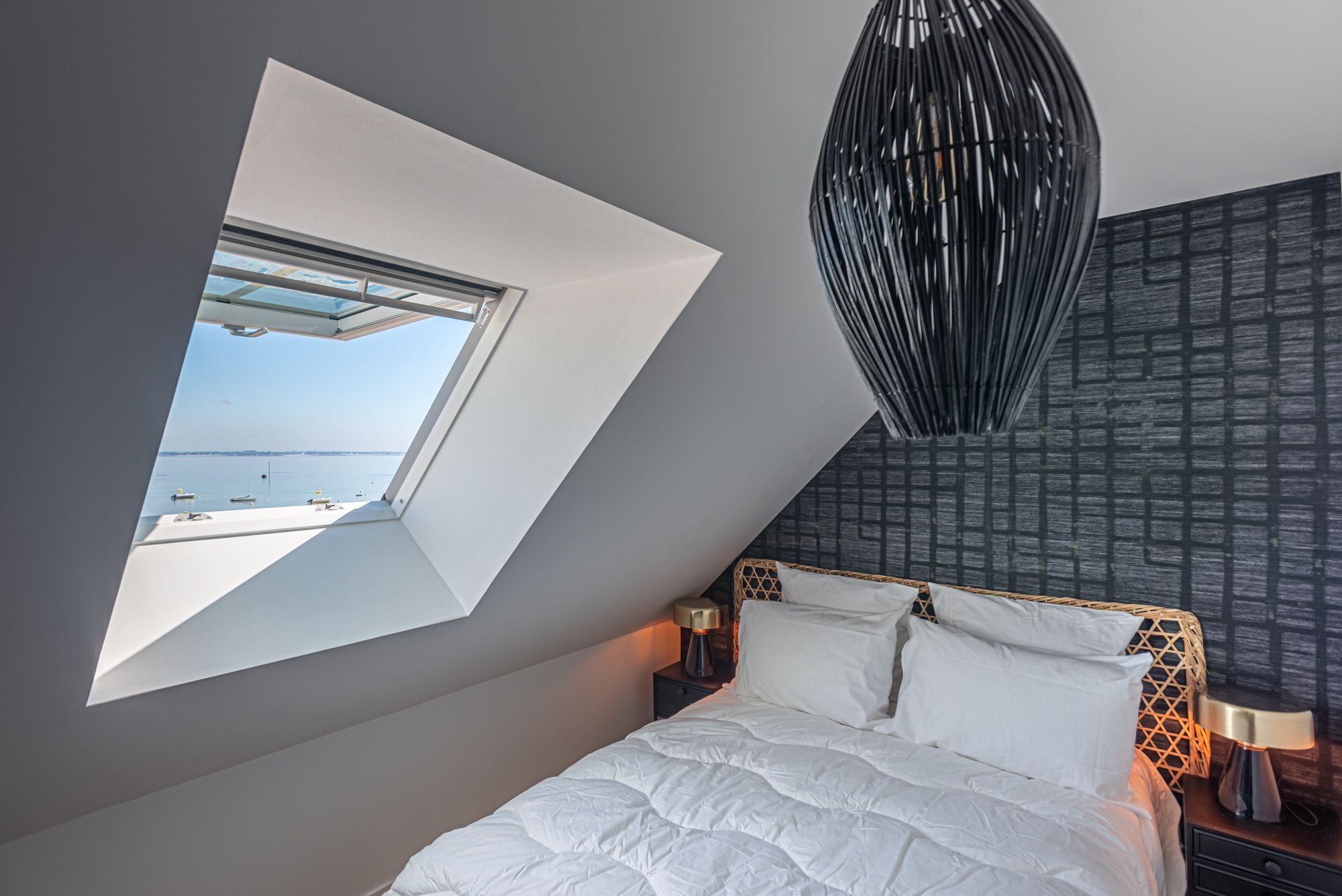 A bedroom with a skylight, a bed, a nightstand, and a wall with a geometric pattern.
