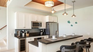 A modern kitchen with white cabinets, stainless steel appliances, a central island with bar stools, and decorative wall art. - Pirates Villa- Beach view with kayaks for Groups (Cruz Bay)