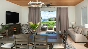 A modern living room with a dining area, a flat-screen TV, a ceiling fan, and a view of the sea. - Pirates Villa- Beach view with kayaks for Groups (Cruz Bay)