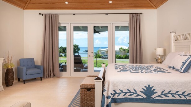 A bedroom with a bed, a chair, a lamp, and a view of the outdoors. - Pirates Villa- Beach view with kayaks for Groups (Cruz Bay)